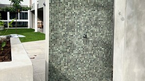 Un edificio moderno con una pared de azulejos, pilares de hormigón y un pequeño árbol.