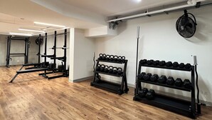 Un gimnasio con suelo de madera, estantes para pesas e iluminación suspendida del techo.