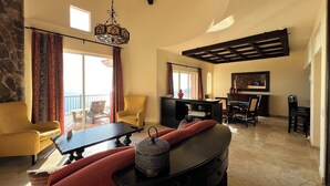 A spacious living room with a sofa, a coffee table, and a fireplace. There is a balcony with a view, and a dining area with chairs and a table. - Cabos Montecristo Villa w/ unobstructed breathtaking ocean view (Cabo San Lucas)