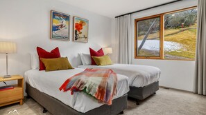 A double bed with red and yellow pillows, a bedside table with a lamp, and a large window with a view of a snowy landscape. - Ski In Ski Out #01 (Ski-In-Ski-Out)