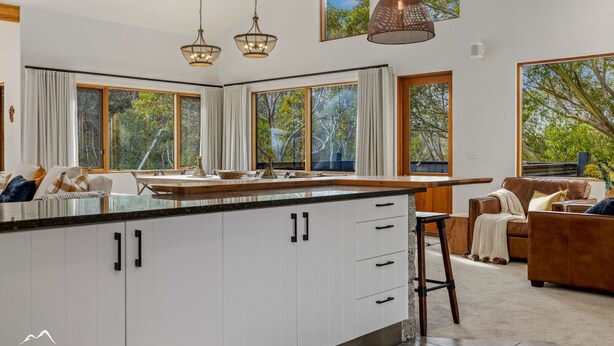 A modern kitchen with large windows, a central island, and a cozy seating area with a leather sofa. - Ski In Ski Out #01 (Ski-In-Ski-Out)
