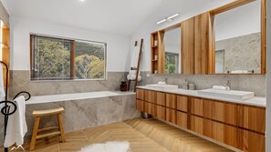 A modern bathroom with a large mirror, wooden vanity, and a bathtub. - Ski In Ski Out #01 (Ski-In-Ski-Out)