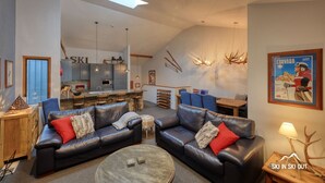 Een moderne woonkamer met leren banken, een salontafel en een keuken in de achtergrond.