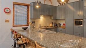 Een moderne keuken met granieten aanrechtbladen, roestvrijstalen apparatuur en houten barstoelen.