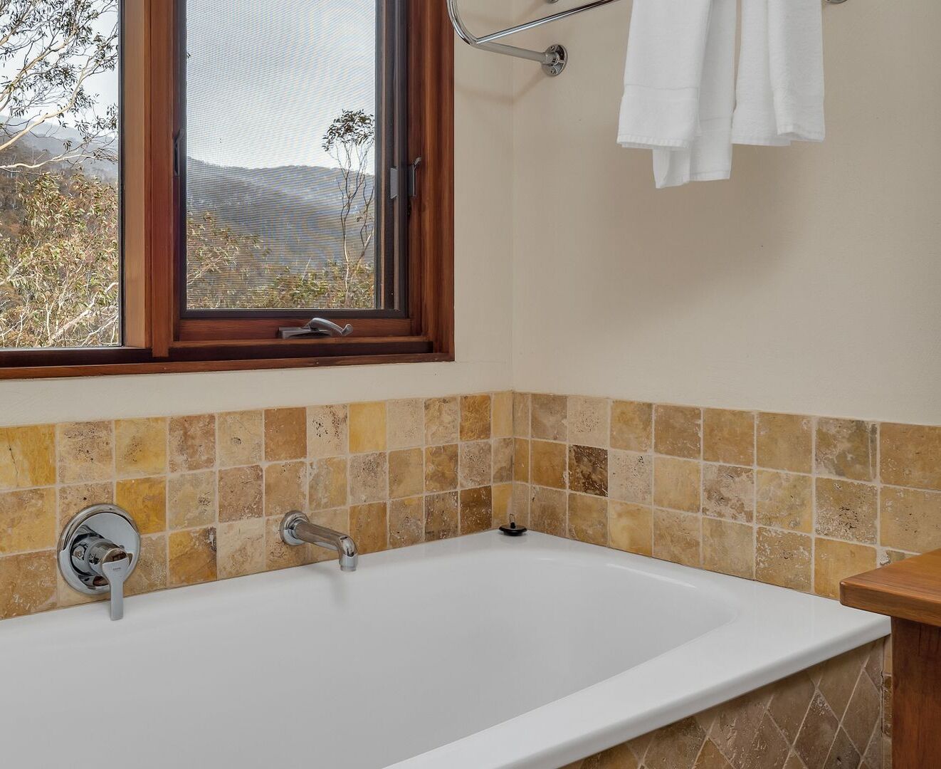 Un baño con una bañera, una ventana que da a árboles y un perchero para toallas.