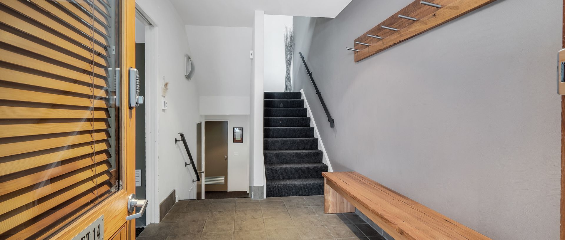 Un interior moderno con una escalera, persianas de madera y un banco.