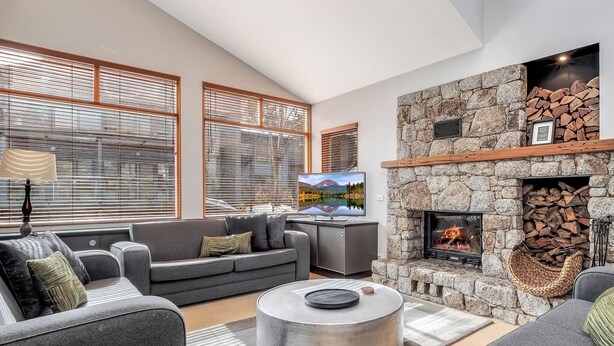 Una sala moderna con chimenea de piedra, sofás grises y televisor de pantalla plana.