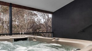 Un jacuzzi con vista a árboles, una pared oscura y una barandilla metálica.