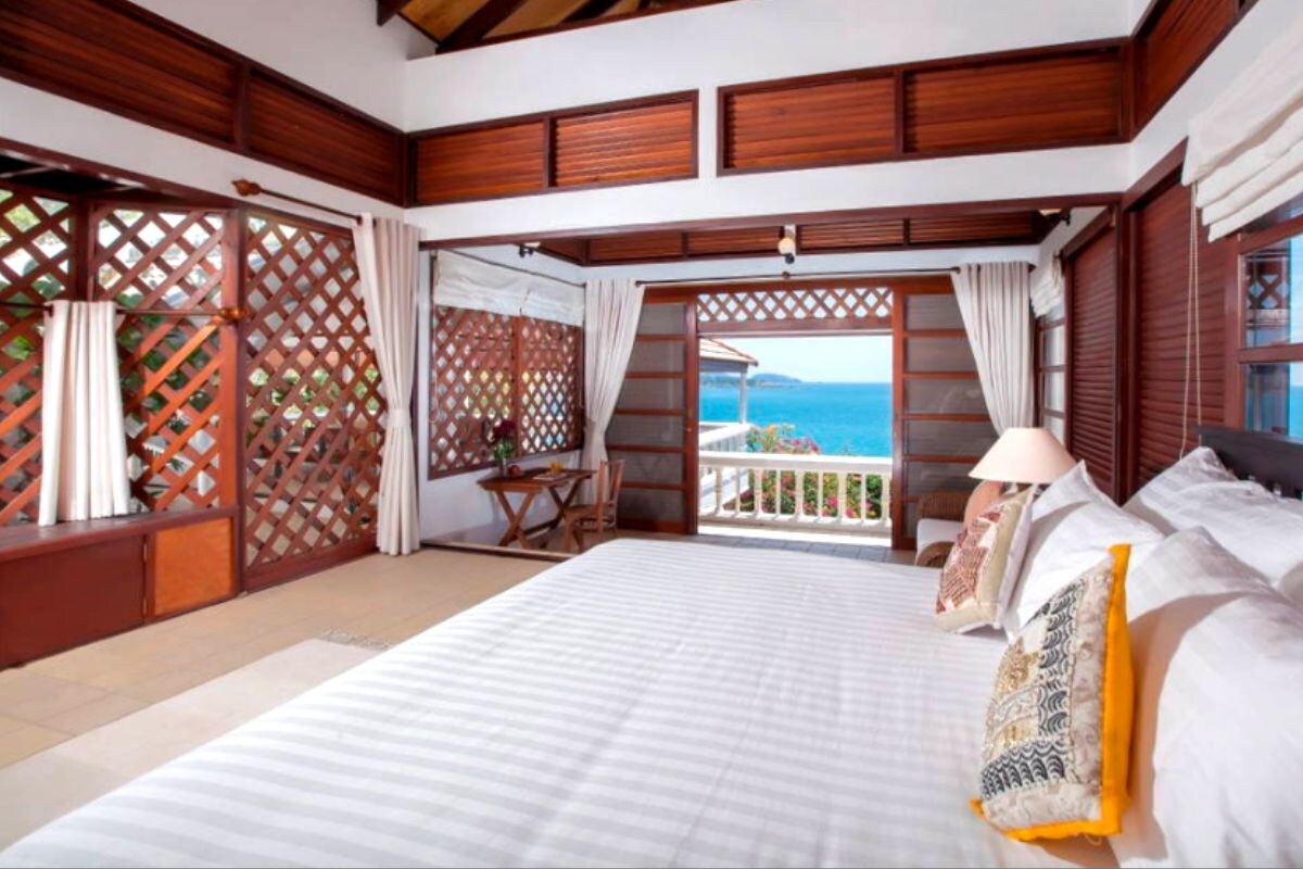 Ein Schlafzimmer mit einem großen Bett, einem Balkon mit Meerblick und Holzvertäfelung.