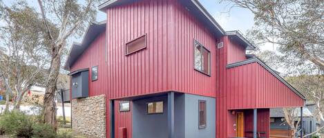 A red and blue two-story house with a stone foundation, multiple windows, and a porch.