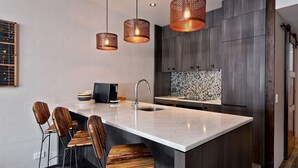 A modern kitchen with a central island, dark wood cabinets, and a mosaic backsplash. - KoKo Nanook - Squatters 15 (Central Village)