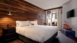 A modern bedroom with a wooden wall, a large bed, a TV, and a suitcase. - KoKo Nanook - Squatters 15 (Central Village)