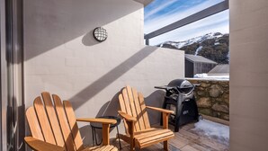 A balcony with two wooden Adirondack chairs, a grill, and a view of a snowy mountain. - KoKo Nanook - Squatters 15 (Central Village)