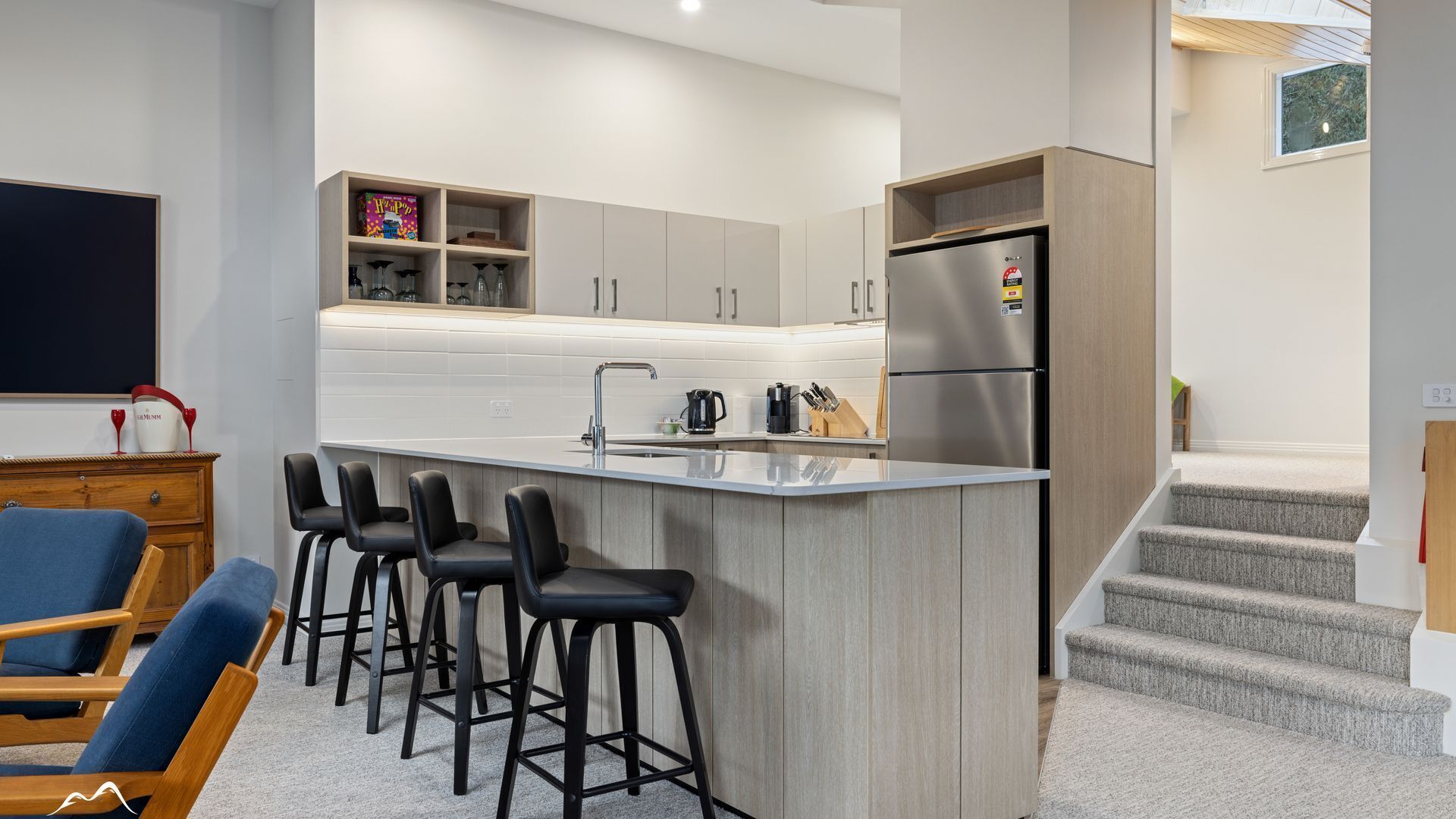 A modern kitchen with a central island, bar stools, a refrigerator, and a dining area with chairs.