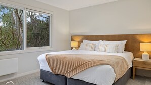 A bedroom with a large window, a bed with white bedding and striped pillows, a wooden headboard, and bedside lamps.