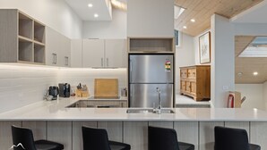 A modern kitchen with a stainless steel refrigerator, wooden cabinets, and a large island with bar stools.