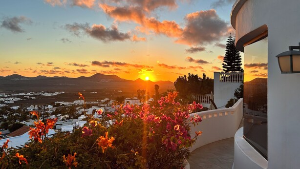 A sunset view from a balcony with a white building, a mountain in the background, and a garden with pink flowers. - Private villa with stunning views and heated pool (Nazaret)