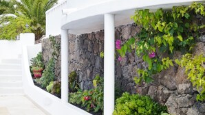 A white building with a stone wall and various plants. - Private villa with stunning views and heated pool (Nazaret)