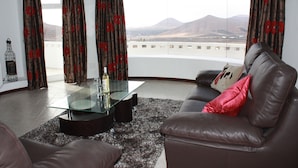 A living room with a glass coffee table, leather sofa, and curtains with a floral pattern. - Private villa with stunning views and heated pool (Nazaret)
