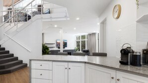 A modern kitchen with white cabinetry, a built-in island, and a staircase leading to an upper level.