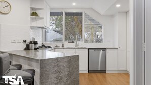 A modern kitchen with a central island, stainless steel appliances, and a view of the outside through large windows.
