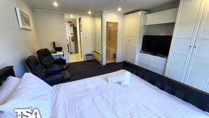Hotellihuone, jossa on sänky, hierontatuoli, televisio ja erillinen vaatehuone.