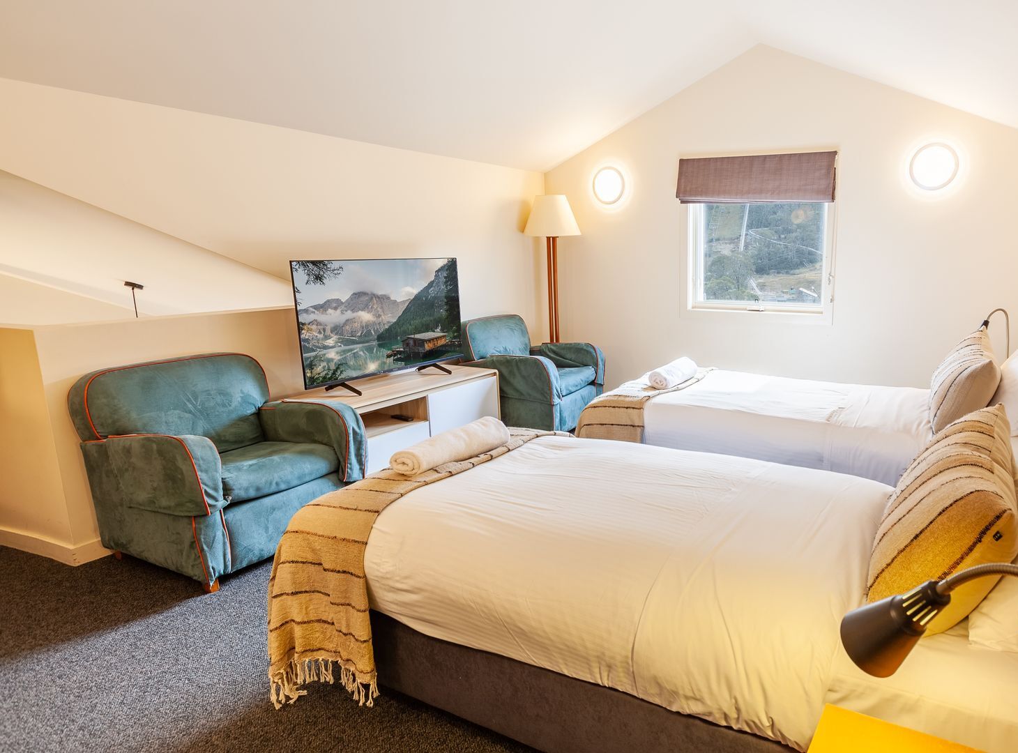 Ein Hotelzimmer mit Fernseher, zwei grünen Sesseln, einem Bett mit weißer Bettwäsche, einem Fenster mit Aussicht und einer Lampe.