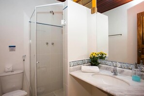 A bathroom with a glass-enclosed shower, a white sink with a marble countertop, and a mirror above the sink.