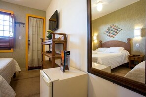 A bedroom with a bed, a small desk, a mirror, and a refrigerator.