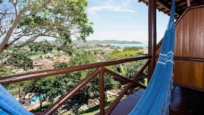 Een hangmat op een houten balkon met uitzicht op een landschap met bomen en een verre blik op huizen.