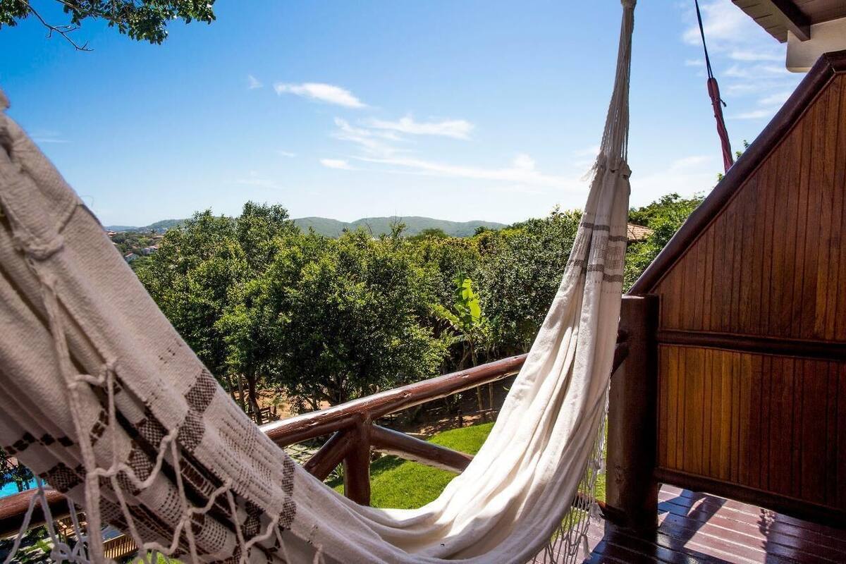 Eine Hängematte auf einer Holzterrasse mit Blick auf eine üppige, grüne Landschaft, Bäume und Hügel im Hintergrund.