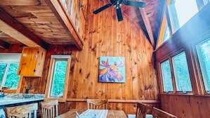 Ein Holzblockhaus-Interieur mit Esstisch, Stühlen, Deckenventilator und einem Bild eines Elchs an der Wand.
