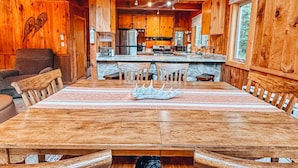 Ein Holzblockhaus-Interieur mit Esstisch, Stühlen, Küchenzeile und einer gemütlichen Sitzecke.