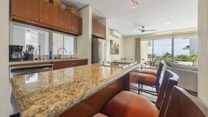 A modern kitchen with granite countertops, wooden cabinets, and a built-in island with bar stools. - 3BR Oceanfront Condo in Sac Bajo (Isla Mujeres)