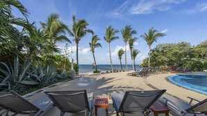 A beachside resort with lounge chairs, a pool, palm trees, and a view of the ocean. - 3BR Oceanfront Condo in Sac Bajo (Isla Mujeres)