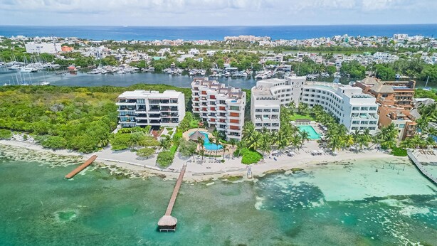 An aerial view of a coastal hotel with multiple buildings, a dock, and clear turquoise waters. - 3BR Oceanfront Condo in Sac Bajo (Isla Mujeres)