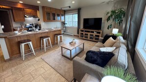 Una sala de estar moderna con un sofá, una mesa de centro y una cocina con armarios de madera y un televisor grande.