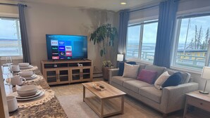 Sala de estar con televisor, sofá, mesa de centro y comedor con platos y vasos.