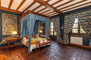 A traditional four-poster bed with a canopy, a wooden bench, a nightstand with a lamp, and a radiator.