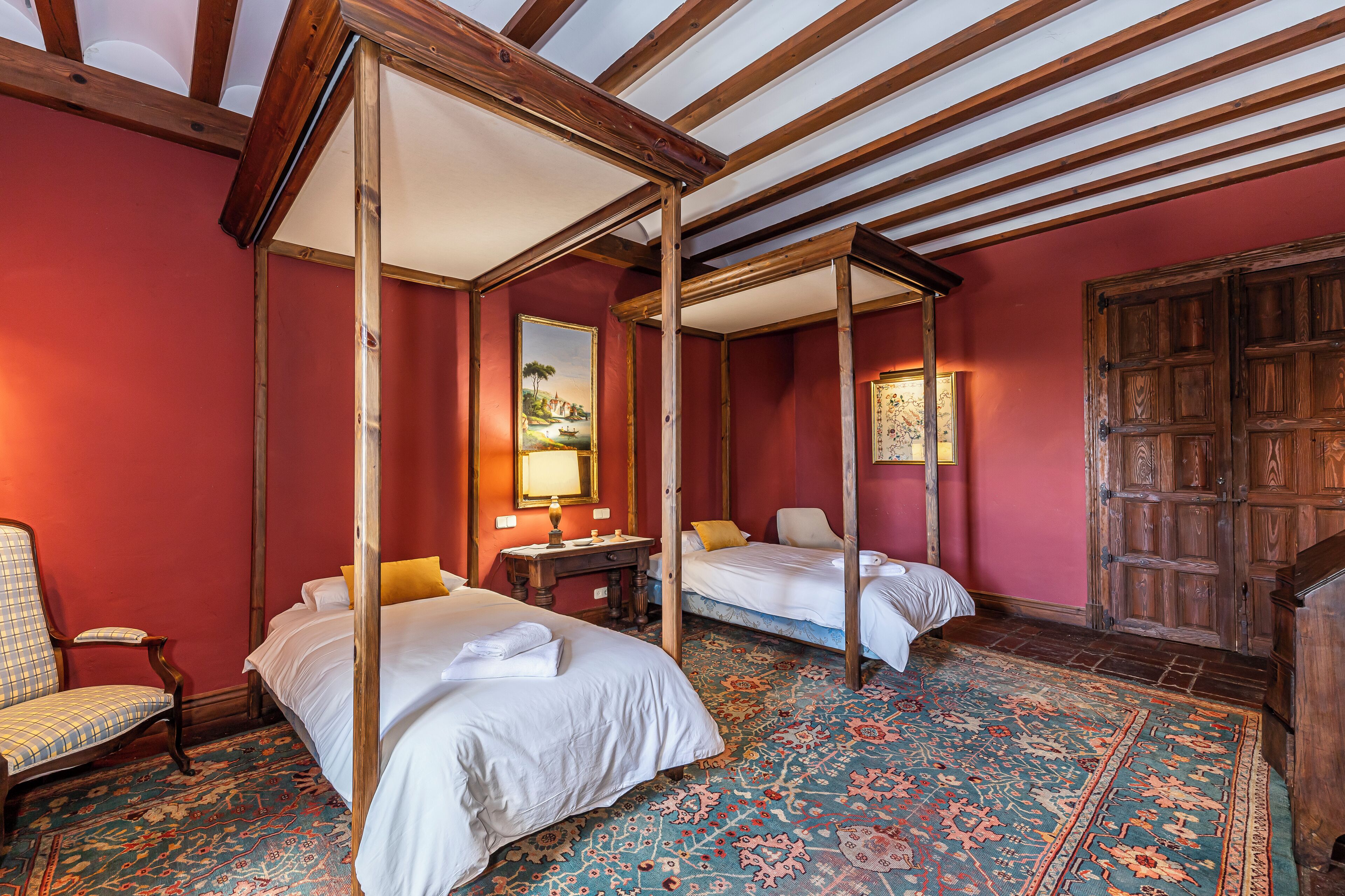 A traditional room with a four-poster bed, a single bed, a wooden wardrobe, and a patterned carpet.