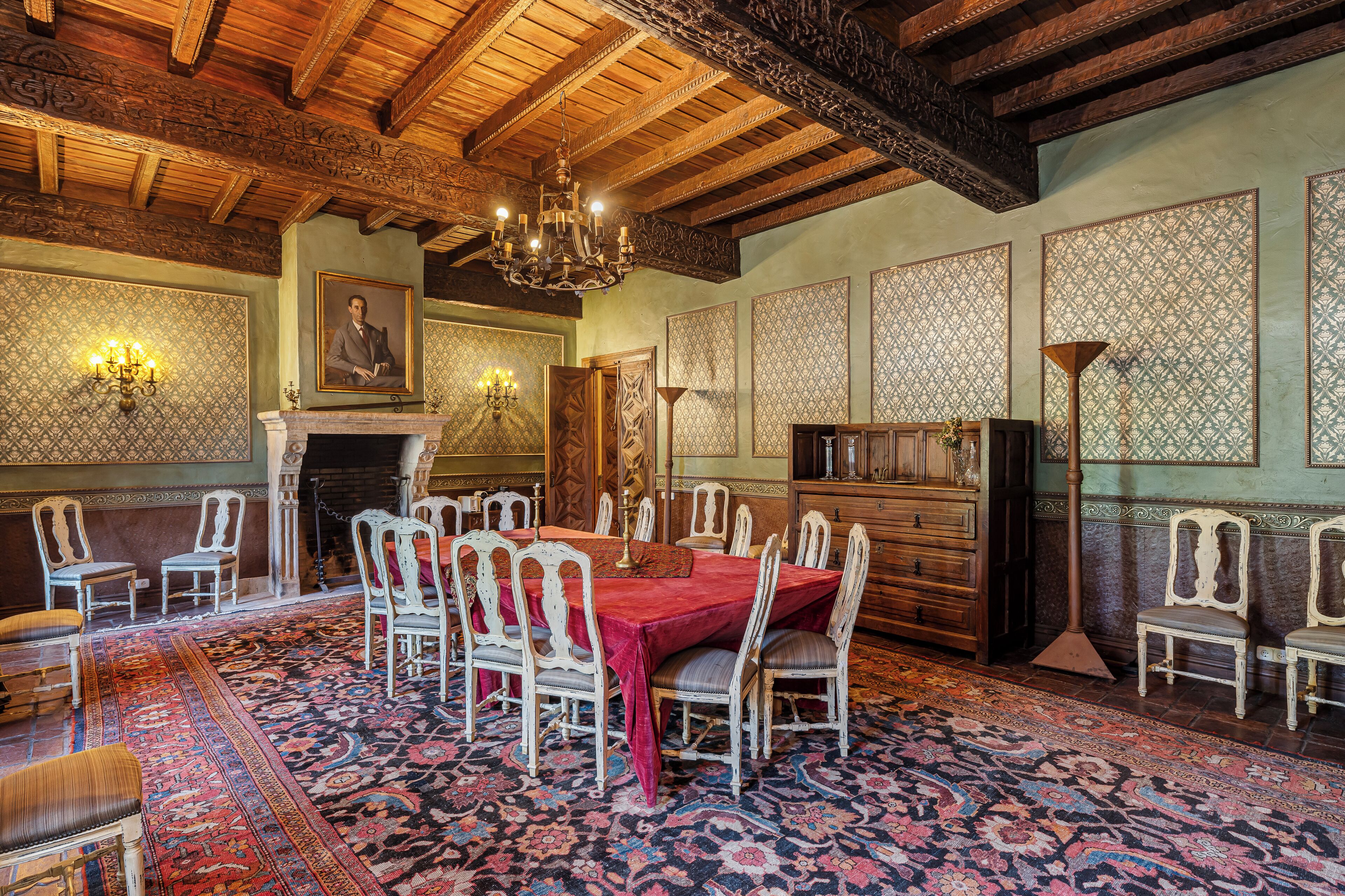 Ein Esszimmer mit einem großen Tisch, Stühlen, einer Kandelaber und Wandverkleidung mit Muster.