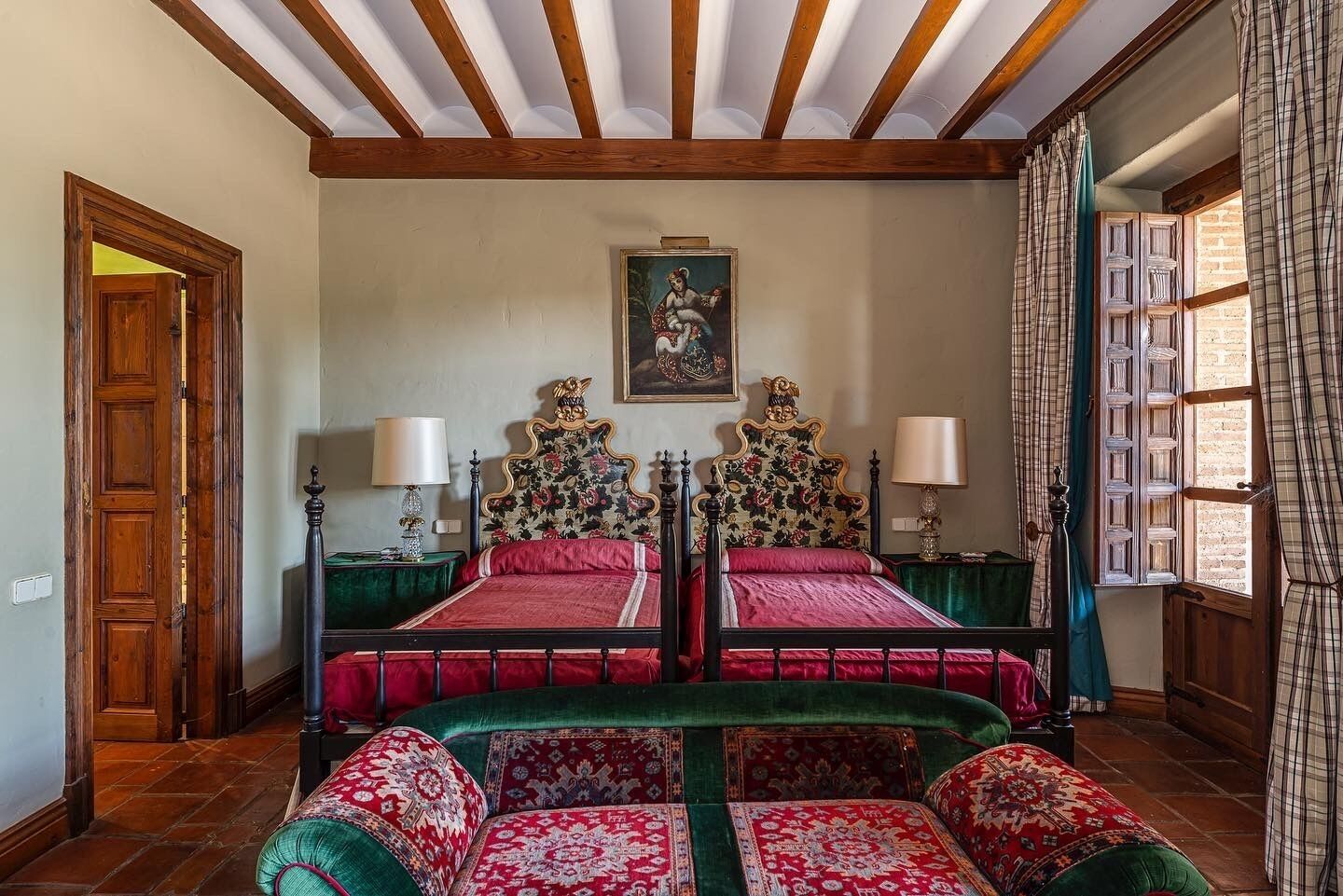 Un dormitorio tradicional con dos camas, un ventanal con cortinas y techo de madera.