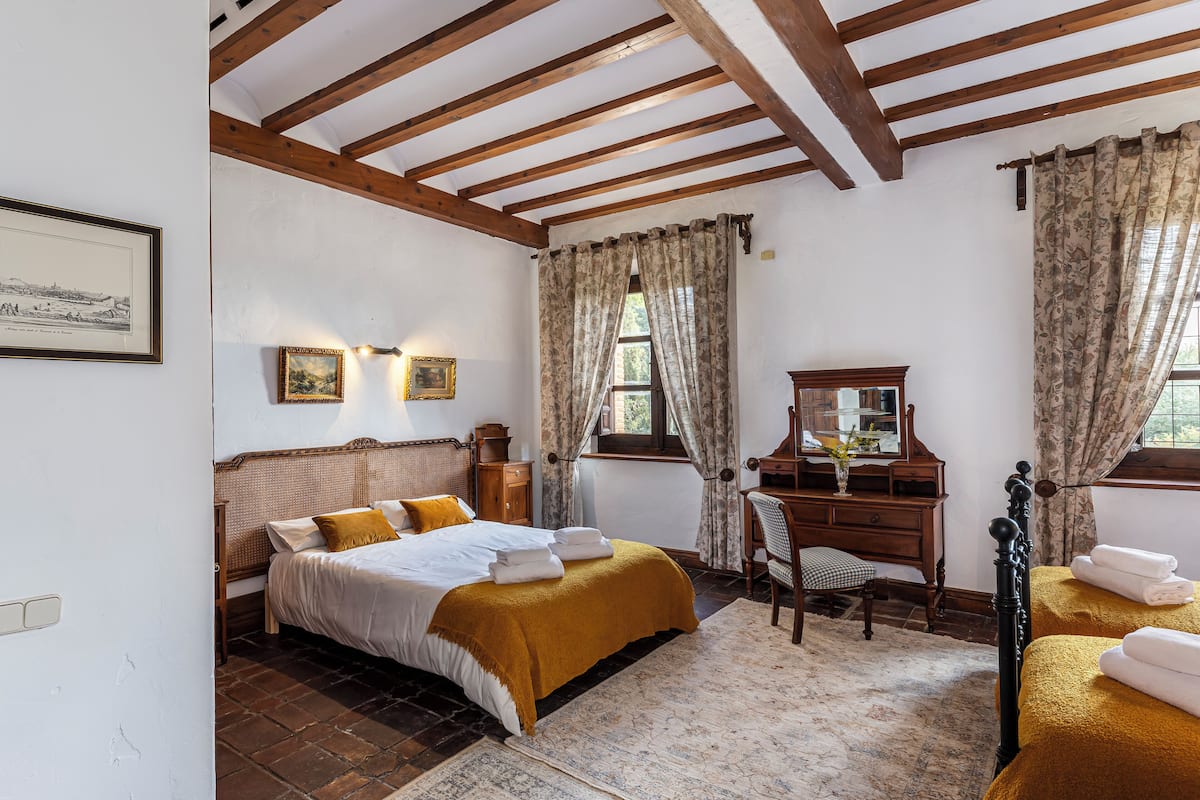 A bedroom with a wooden ceiling, a bed with white bedding, a wooden dresser, and a window with curtains.