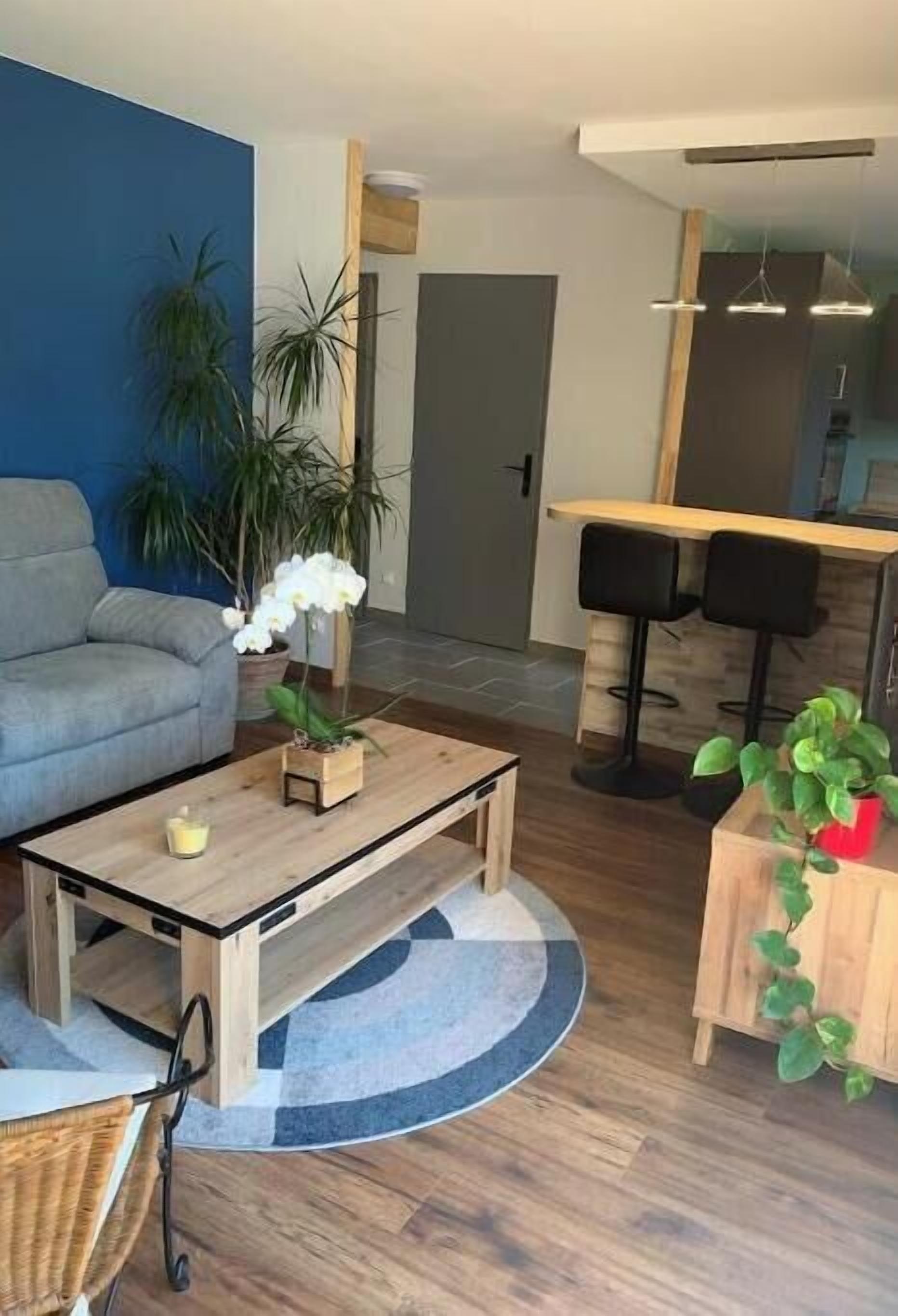 A modern living room with a grey sofa, wooden coffee table, and a dining area with two black bar stools.
