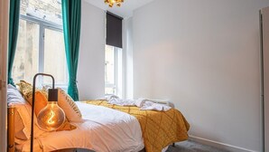 A bedroom with two beds, a hanging light fixture, and a window with curtains. - Blissfully Peaceful 1 Bed Flat In Crown Street (West Yorkshire)