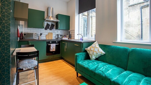 A compact kitchen with a green sofa, a dining table, and a window providing natural light. - Blissfully Peaceful 1 Bed Flat In Crown Street (West Yorkshire)