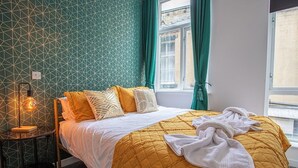 A neatly made bed with a yellow quilt, a bedside lamp, and a patterned wall. - Blissfully Peaceful 1 Bed Flat In Crown Street (West Yorkshire)