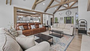 A spacious living room with a high ceiling and exposed beams, featuring a brown leather sofa, a white sofa, and a coffee table.