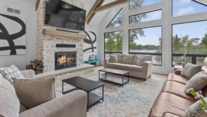 A modern living room with a stone fireplace, large windows, a sofa, and a coffee table.