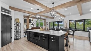 A modern kitchen with a large island, wooden beams, and pendant lighting.